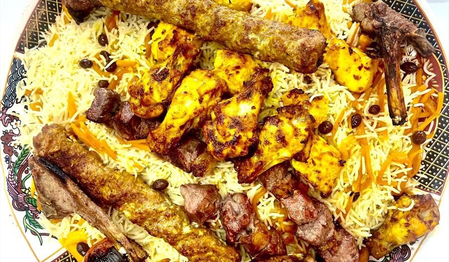 A large decorative platter filled with yellow rice topped with various grilled meats, including kebabs, chicken, and lamb chops, as well as roasted to