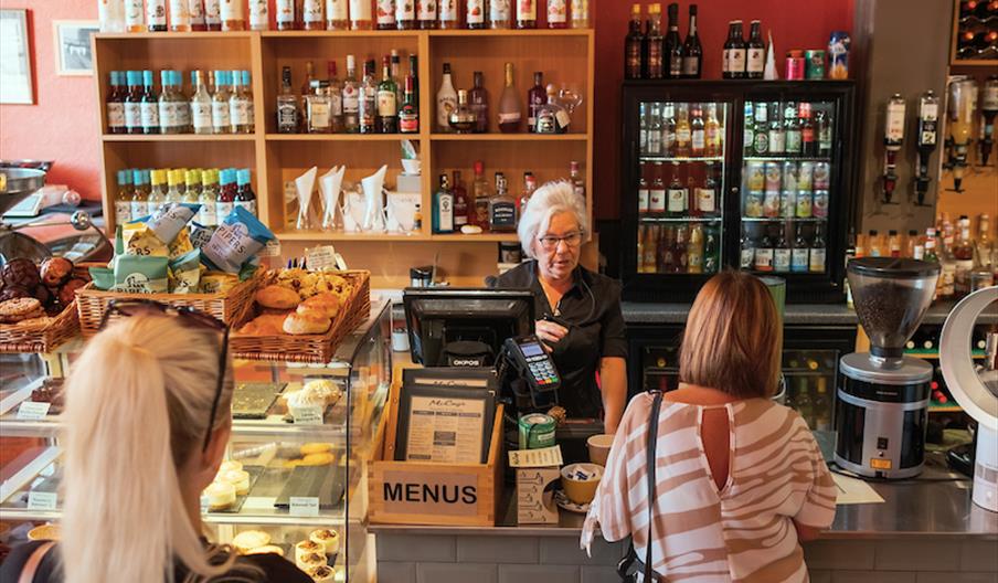 Interior of McCoys. A bakery and coffee shop counter with pastries and baked goods displayed in glass cases, shelves of syrups and liquor bottles behi