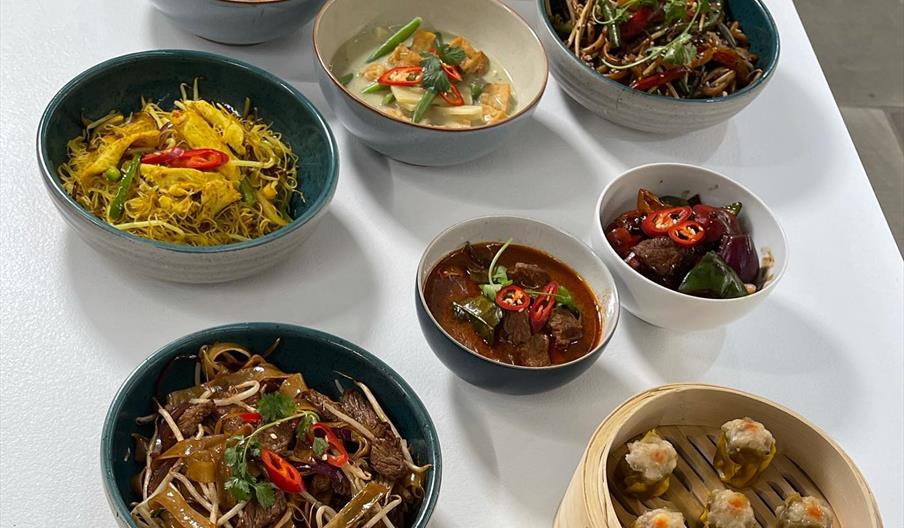 An array of Asian dishes in various bowls and bamboo steamers on a white table.