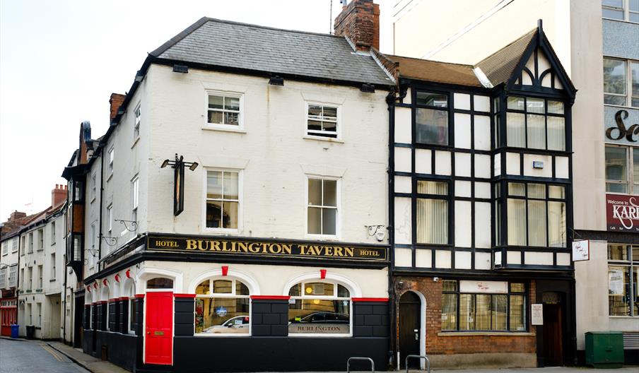 A street view of the Burlington Tavern, a traditional British pub and hotel with a black and white exterior, arched windows, and a bright red door on