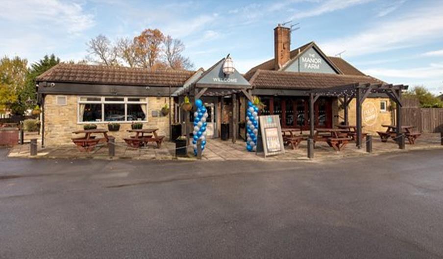 A wooden table set with various Italian dishes, including a pizza topped with arugula and prosciutto, a pasta dish, breaded fried sticks with greens,