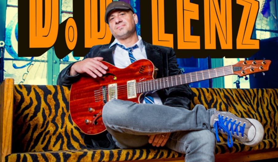 A man wearing a cap and casual clothes sits on a zebra-print bench holding an electric guitar, with text promoting a B.D. Lenz jazz show at The New Ad