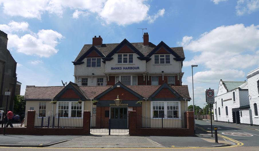 Exterior of large pub painted cream with grey door and black  metal fence.