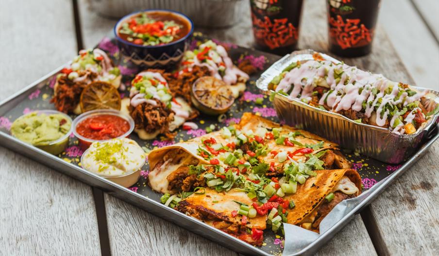 A metal tray filled with different types of mexican food, such as quesadillas, burritos and various dips.
