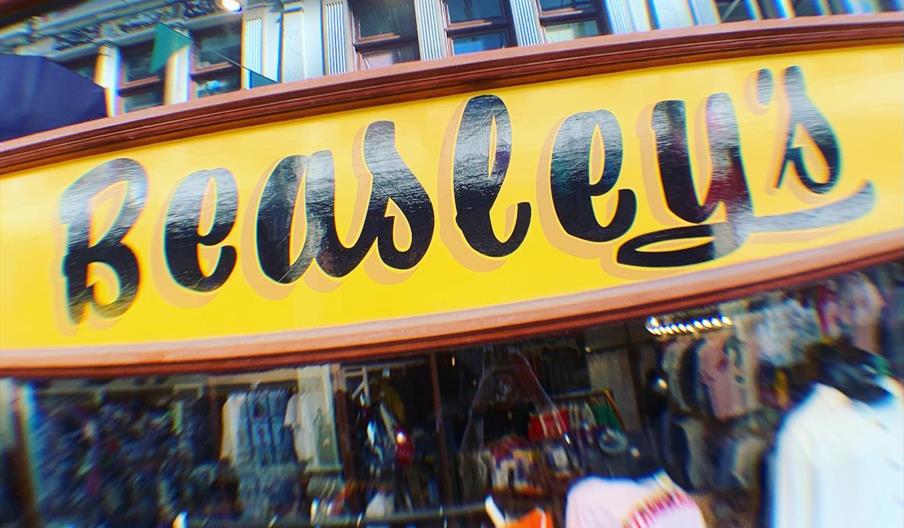 A storefront with a large yellow sign reading "Beasley's" in bold black script lettering; below the sign, various racks of clothing are visible throug