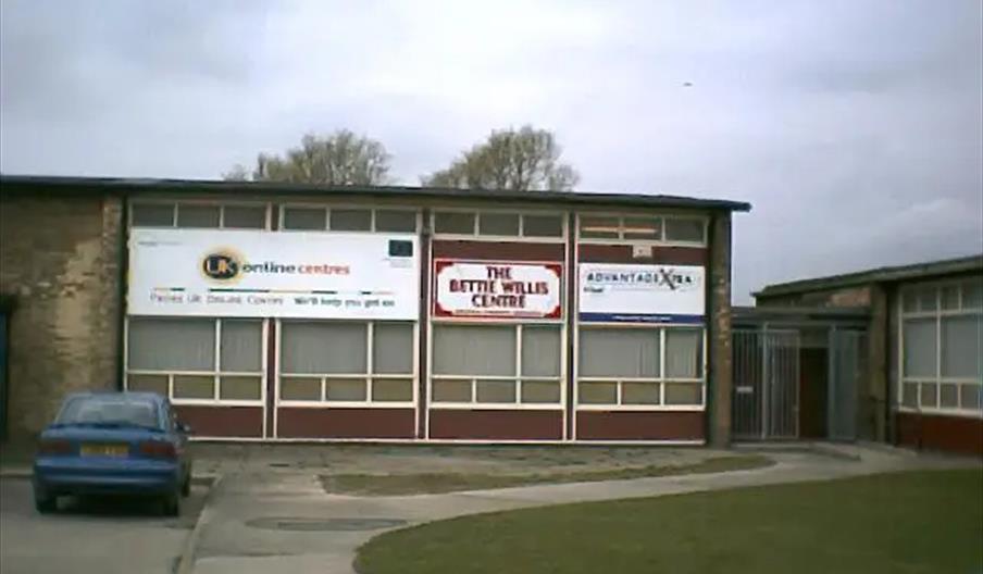 A single-story building with large windows and three prominent signs on the front, including one that reads "THE BETTIE WILLIS CENTRE," with a blue ca