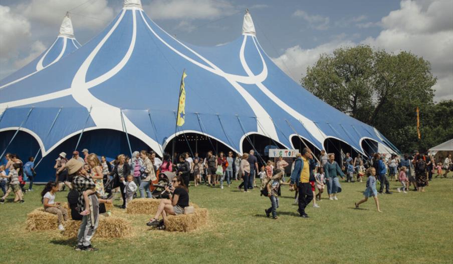 A large crowd of people, including families with children, gather outside a large blue and white festival tent labeled "Big Top" at the Big Malarkey F