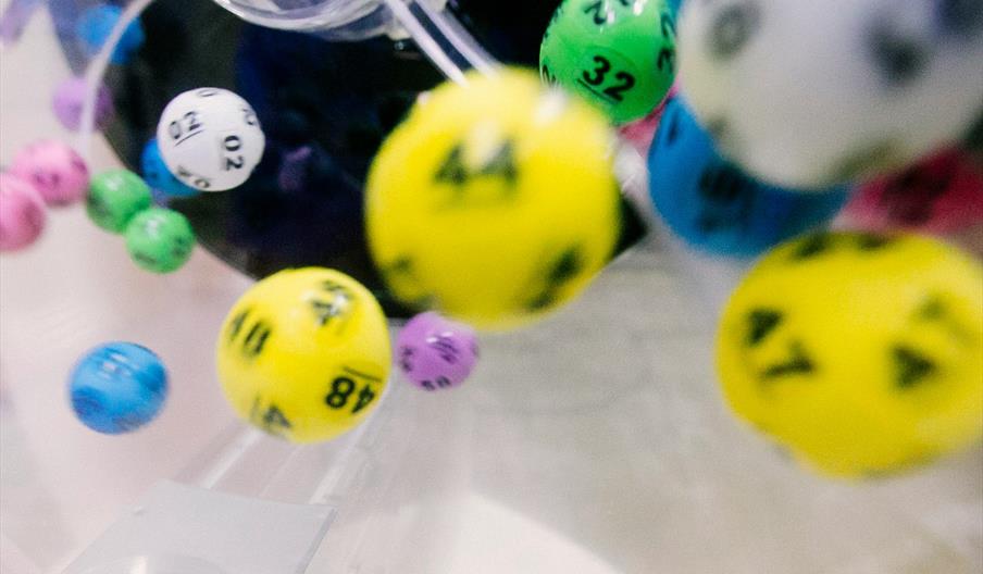 Close-up view of colorful lottery balls, including yellow, green, blue, purple, and white, swirling inside a transparent lottery machine.