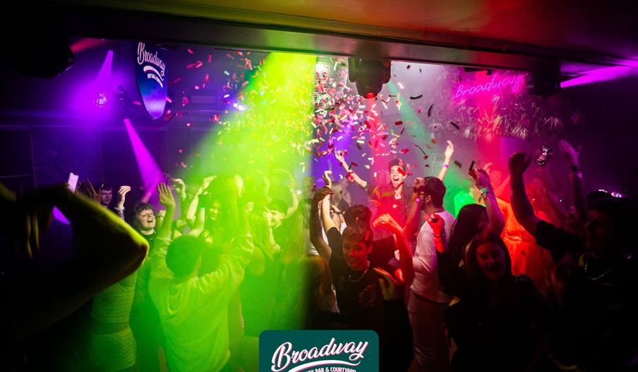 A group of young people clubbing in Broadway Party Bar & Courtyard with multicoloured streamers and a discoball.