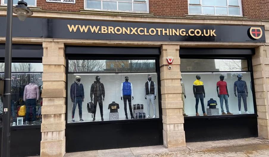 Street view of the Bronx Clothing store with large display windows featuring mannequins dressed in men's casual and sporty outfits, including jackets,