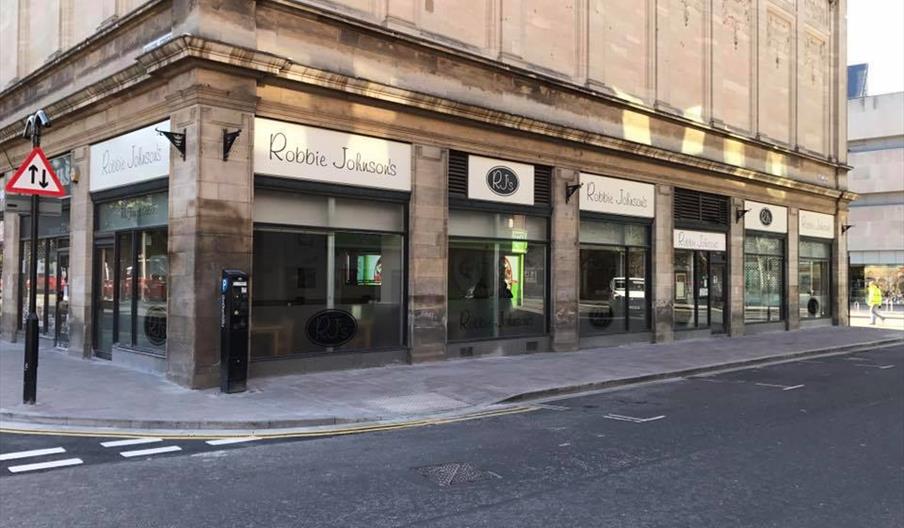 Exterior of Robbie Johnson's restaurant on a city corner, featuring large glass windows and a stylish facade with signage.