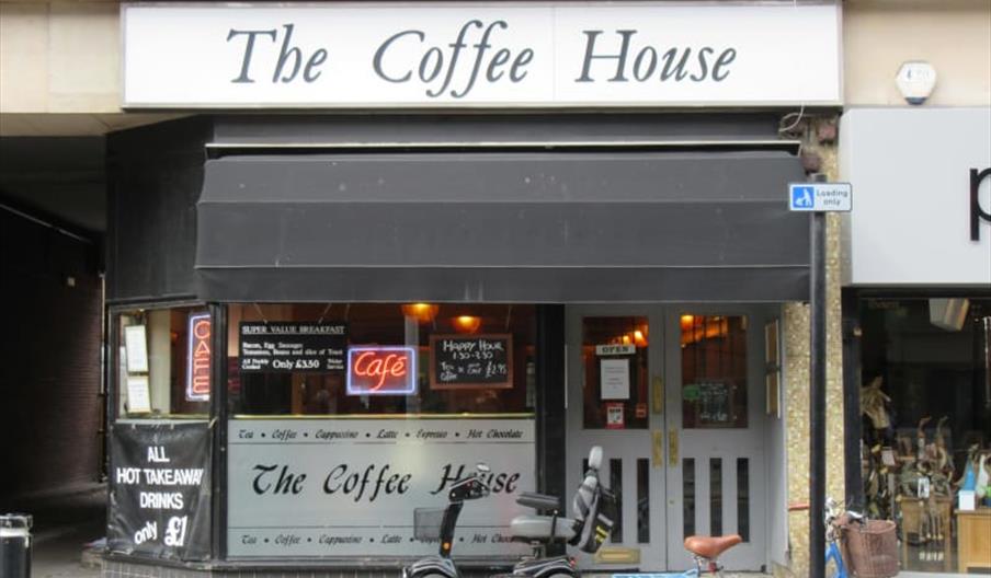Street view of The Coffee House café with a black awning and glass windows, a mobility scooter parked in front, and a blue bicycle leaning against a p