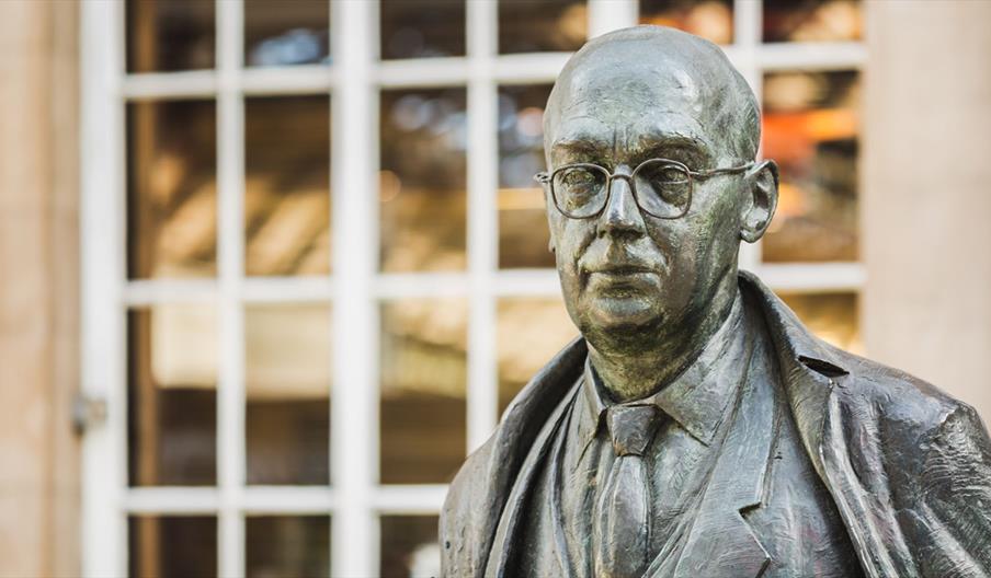 A statue of Philip Larkin, a man with fine glasses and dressed in a suit with an overcoat.