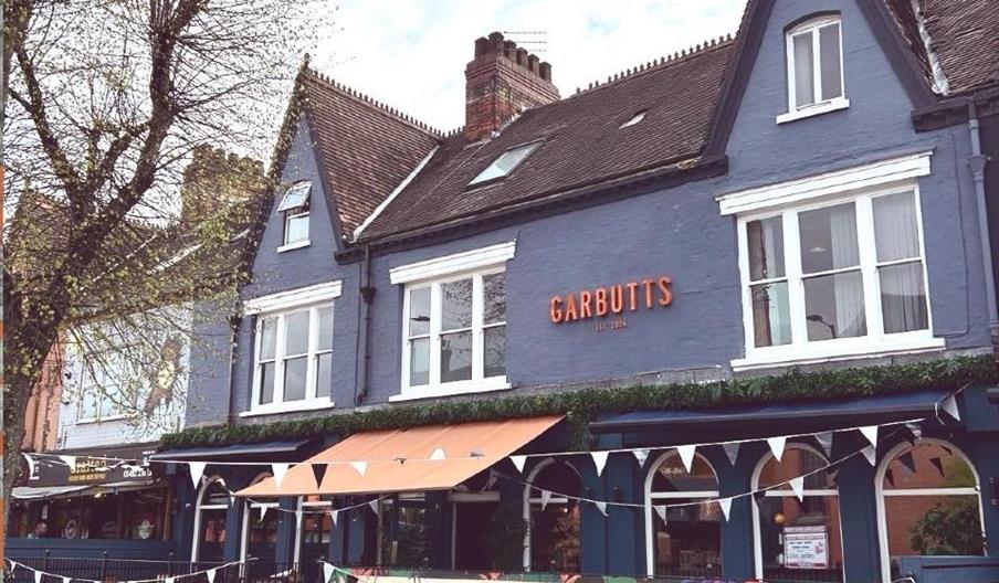 A blue Victorian-style building with pointed roofs and white trim houses "Garbutts," a bar and restaurant. The exterior is decorated with bunting and