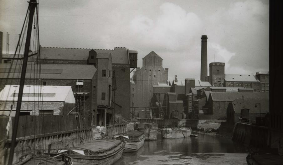 A black and white photograph taken by William Jackson showing a stretch of the River Hull in the 1930s. Barges are crowded along either bank while mil