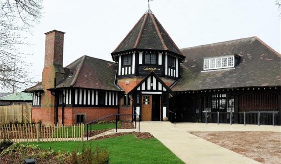 A historic building with a central octagonal tower, half-timbered upper walls, brick lower walls, and a steeply pitched roof. There is a paved walkway