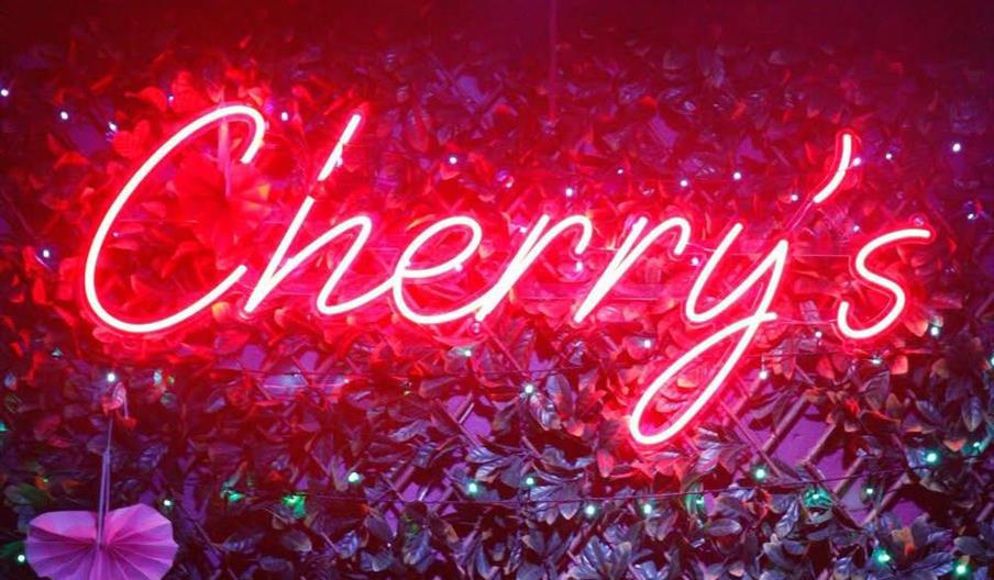 A red neon light reads 'Cherry's' on a wall decorated with leaves.