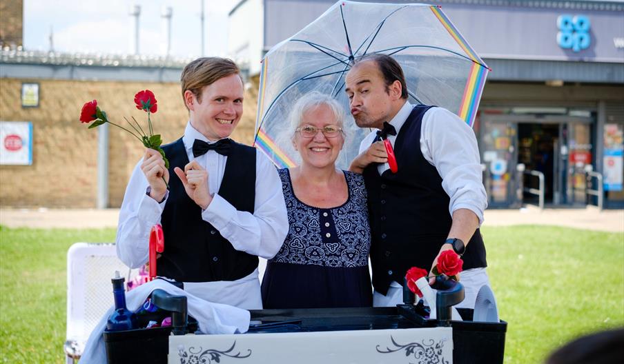 Two waiters pose with an elderly lady outside.