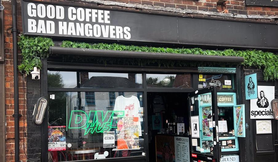 The exterior of a quirky coffee shop with a sign above the entrance reading "GOOD COFFEE BAD HANGOVERS" in bold white letters. The storefront features