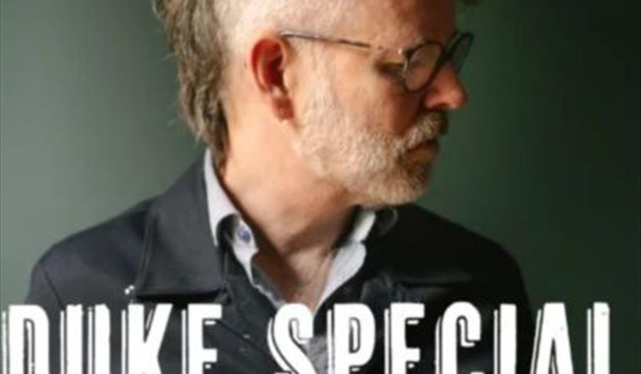 A man with glasses and a styled mohawk hairstyle looks to the side against a dark background. Large text reads "Duke Special," and below it, details f