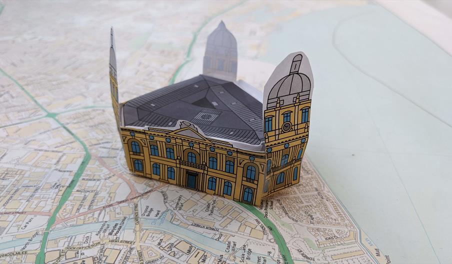 A small papercraft version of the Hull Maritime Museum, a historic building with multiple windows and three domed towers sits on a streetmap of Hull.