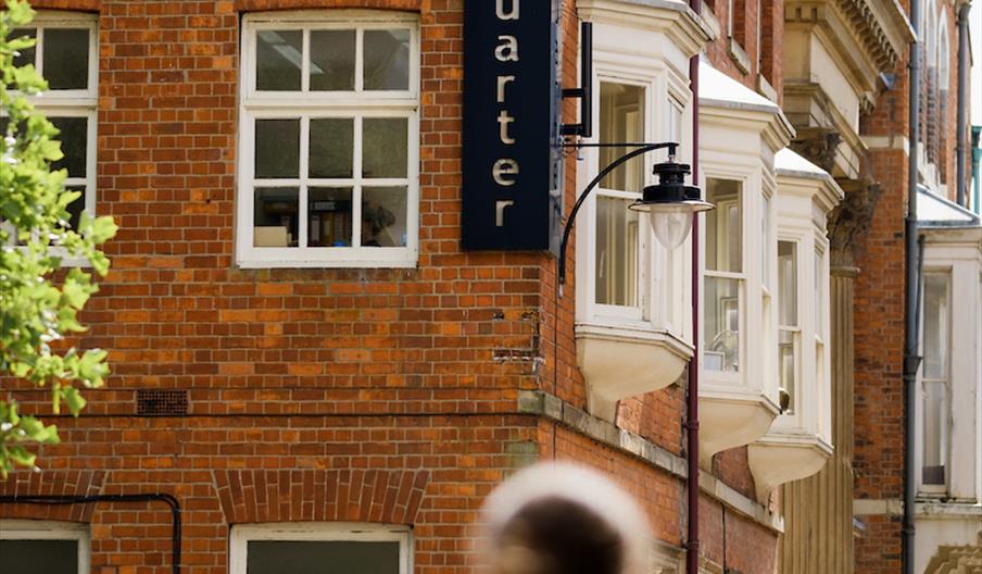 A person walks down a street with victorian architecture with a large sign on the corner of the building reading 'The Museum Quarter'