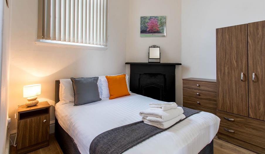 Bedroom with bouble bed, white linen and orange cushions.