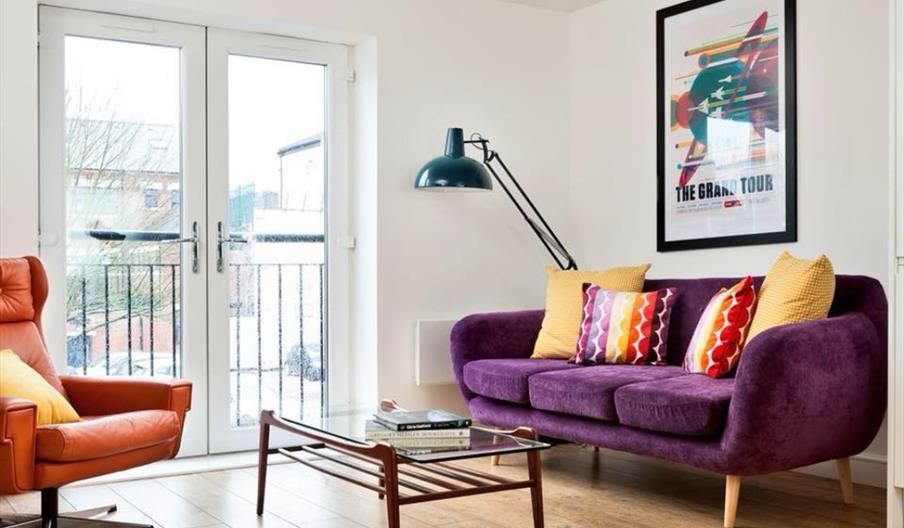 Lounge area with wooden floors, purple sofa and orange armchair.