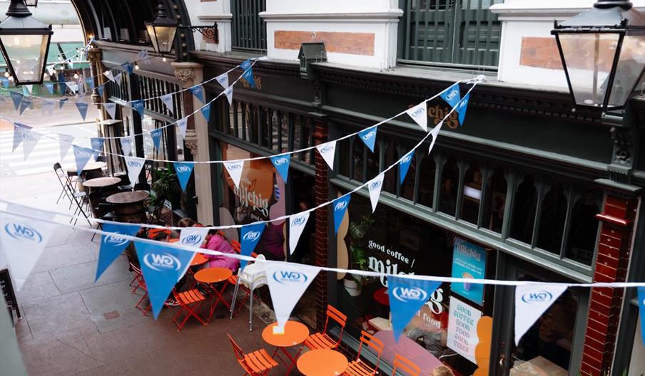 A view from one of the upstairs windows in Paragon Arcade, a victorian shopping arcade. Looking down on the scene, people are eating at bright orange