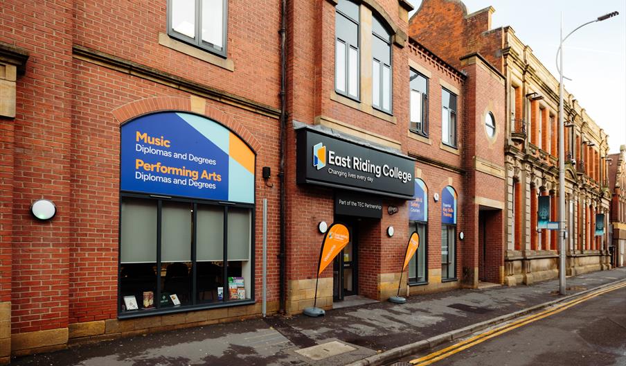 Street view of the red-brick East Riding College building, with prominent signage advertising Music and Performing Arts programs, and the main entranc