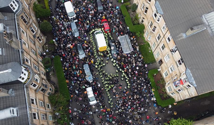 Top-down aerial photograph of a crowd of people surrounding a van in Kenmure Street in Glasgow.