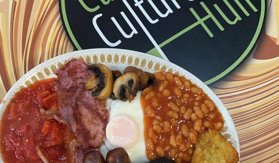 A full English breakfast on a white plate with a slice of white toast on the side on a wooden table.
