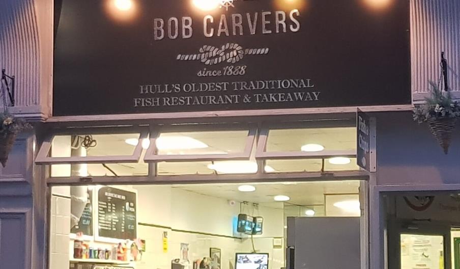 Exterior of fish and chip shop with large window and illuminated sign.