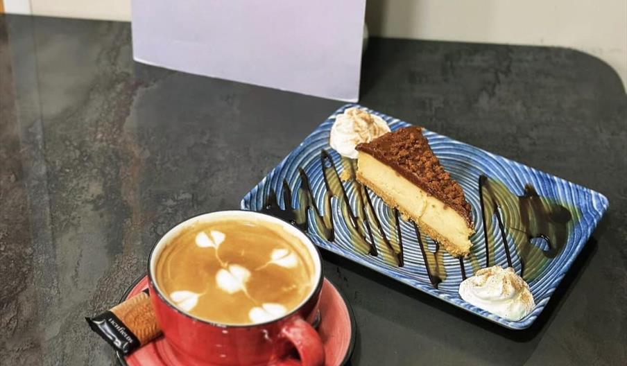 Coffee in a red cup with a slice of cake on a blue plate and menu.