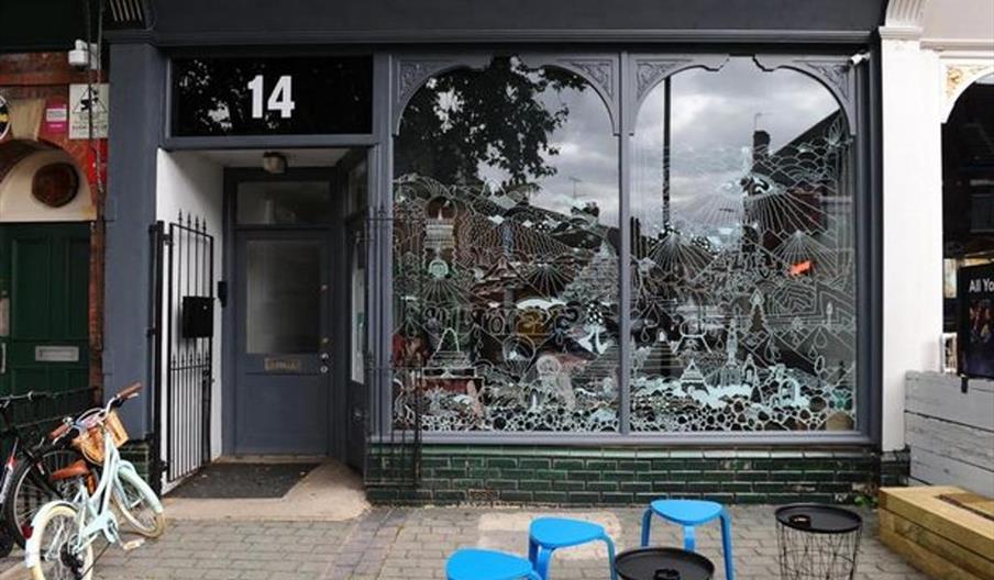 Exterior of bar with large, hand decorated windows and blue metal stools.