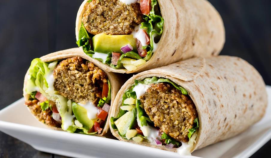 Three falafel rolls with cucumber, herbs and dressing on white plate.