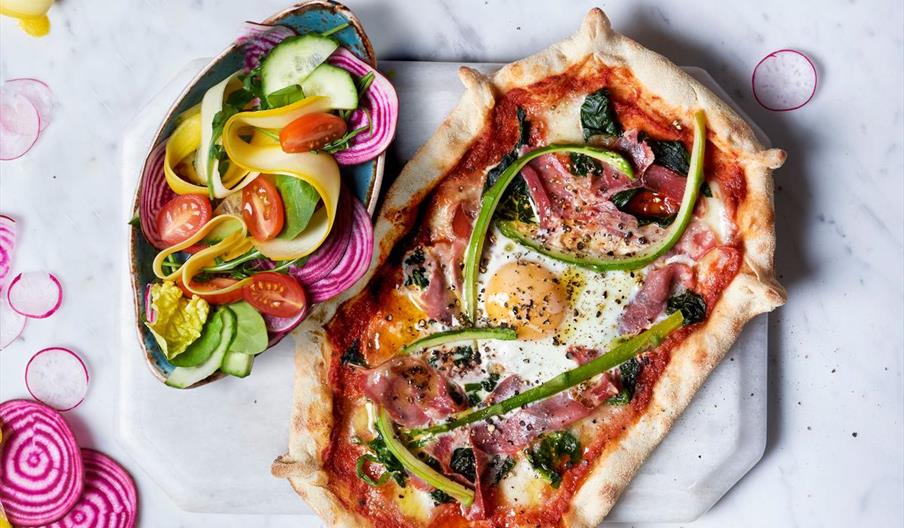 Pizza with ham, spinach and egg, along with a side salad.
