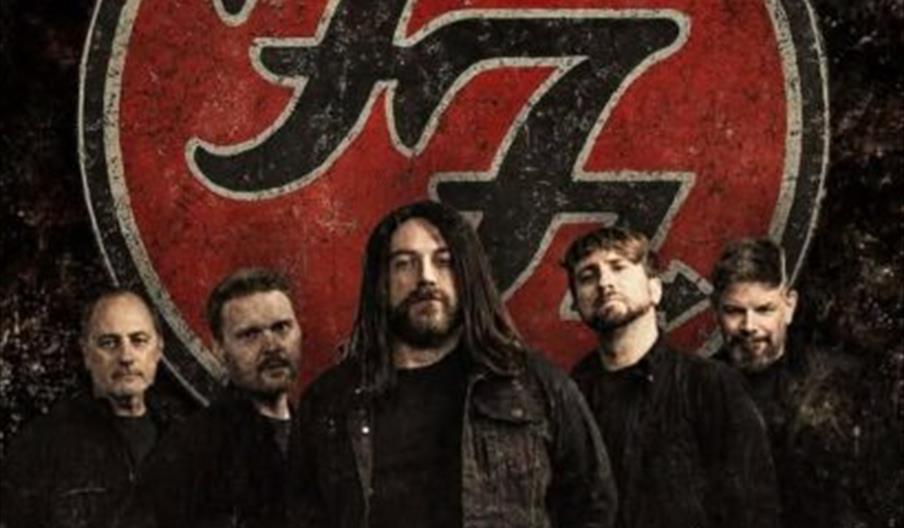 Five men stand in front of a large red and black Foo Fighters logo, with the words "Hull O'Rileys" displayed at the bottom of the image.