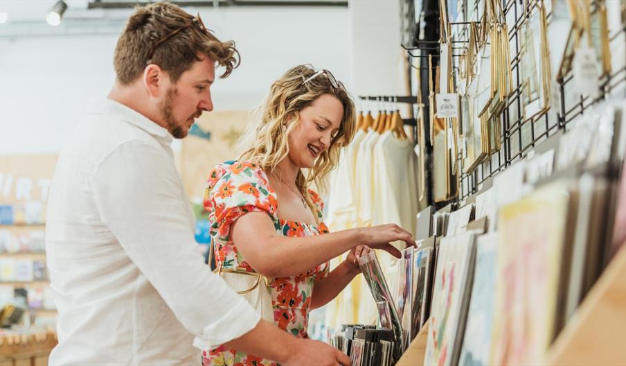 Two people browsing art prints and stationery displayed on a wall rack inside Form Shop and Studio, a creative retail space featured by Visit Hull.