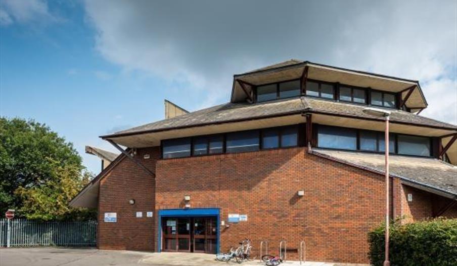 A brick building with a modern, layered roof and large upper windows, identified as the Fred Moore Library. There are bicycle racks with bikes in fron