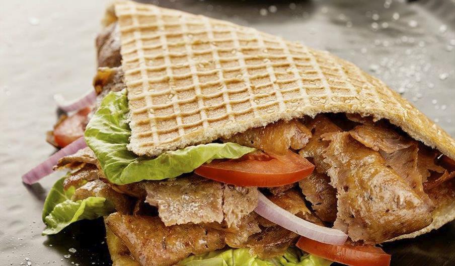 A large doner kebab, filled with lettuce, tomatoes, and other toppings.