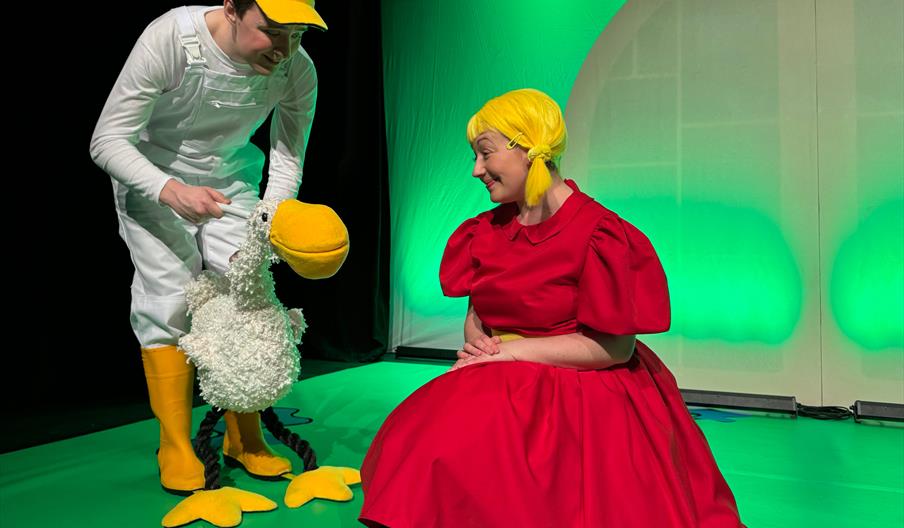 A puppet white goose and a small girl in a red dress say hello