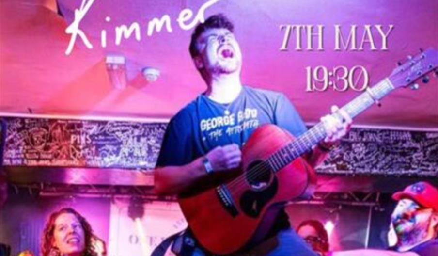 A musician passionately plays an acoustic guitar on stage surrounded by colourful lights and an energetic audience, with event details overlaid: "Harr