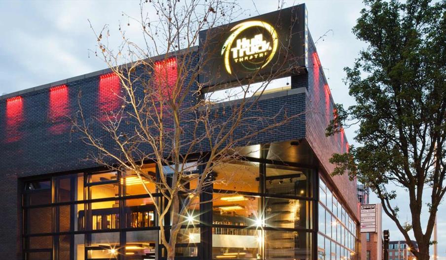 The exterior of Hull Truck Theatre, a black brick building with 2 glass sided walls. 2 trees stand either side of the main entrance.