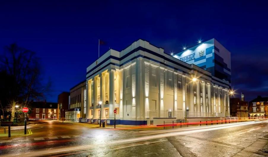 The exterior of Hull New Theatre at night, a large white building with pillars framing the main entrance.