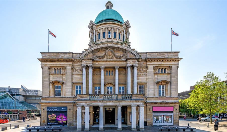 The Exterior of Hull City Hall, a large ornately decorated building made out of sandstone, with a green dome on the roof. Several pillars line the fro