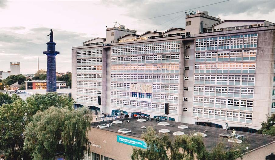 A large, multi-story modern building, Hull College with many windows stands behind a shorter building marked with a sign that reads "The Creative Hear