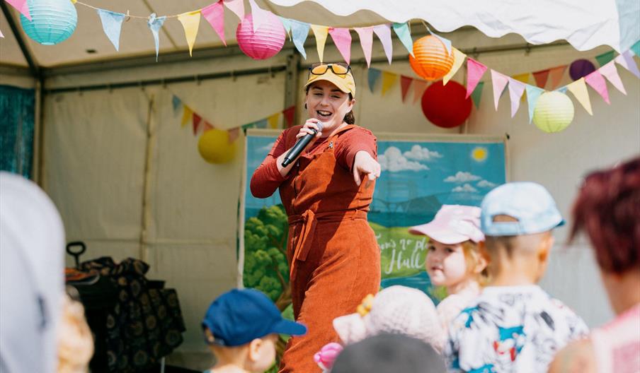 A lady poses with a microphone in front of several children.