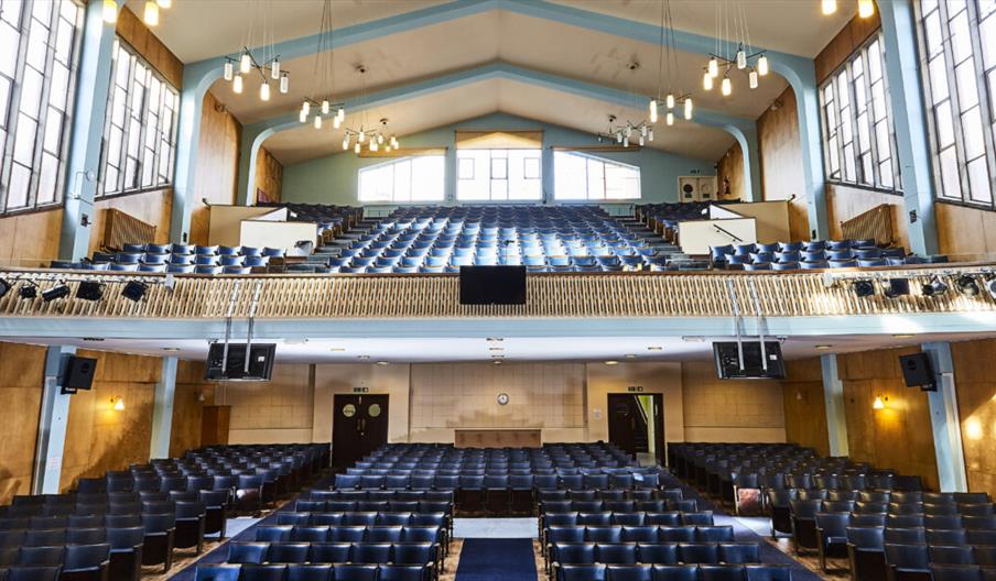 Jubilee Central is a spacious auditorium with rows of navy blue seats on the ground floor and a balcony, large windows lining the walls, and modern ha