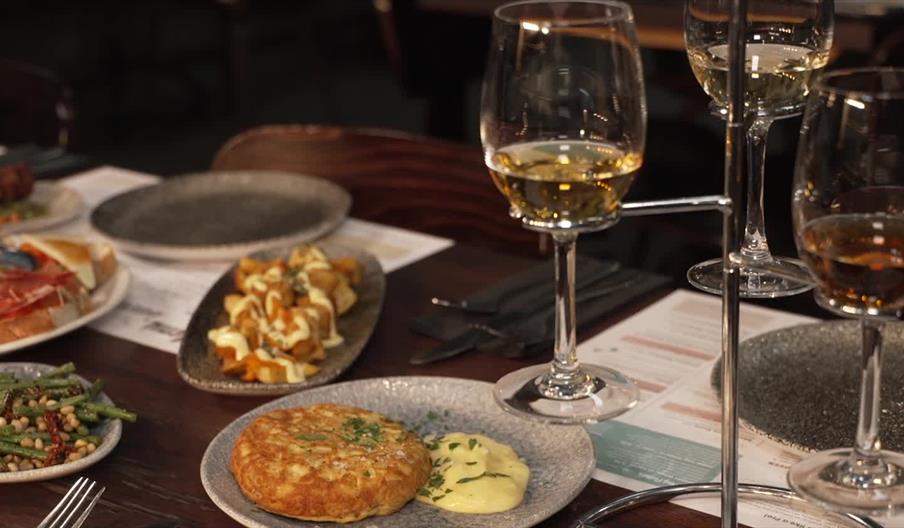 Table set with a selection of tapas-style dishes, including toasted bread with cured meats and olives, green beans with pine nuts, patatas bravas, and